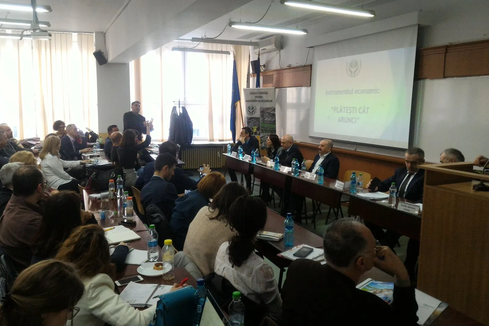 Ecran de proiecție cu titlul „Instrumentul economic «Plătești cât arunci»” și roll-up-ul Asociației Române pentru Managementul Deșeurilor, la dezbaterea din 29 martie 2018