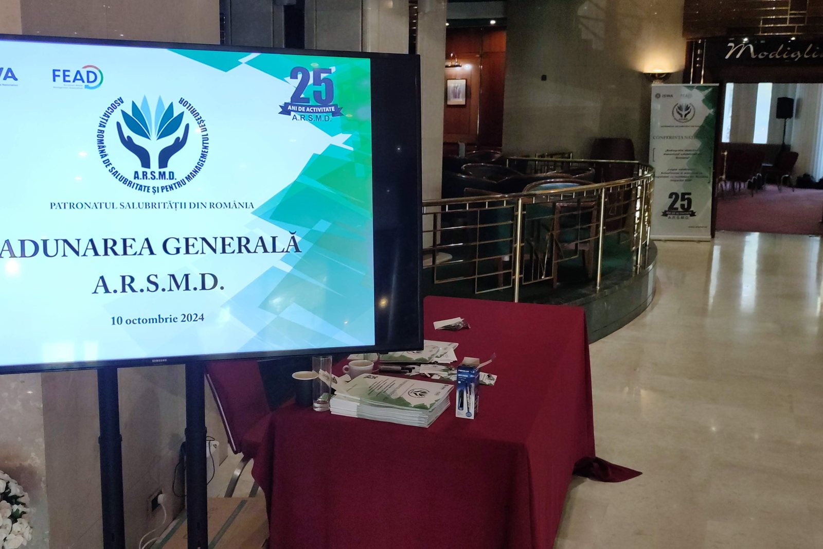Ecran cu însemnul Adunării Generale A.R.S.M.D. din 10 octombrie 2024, în foaierul sălii Rapsodia a Grand Hotel Bucharest