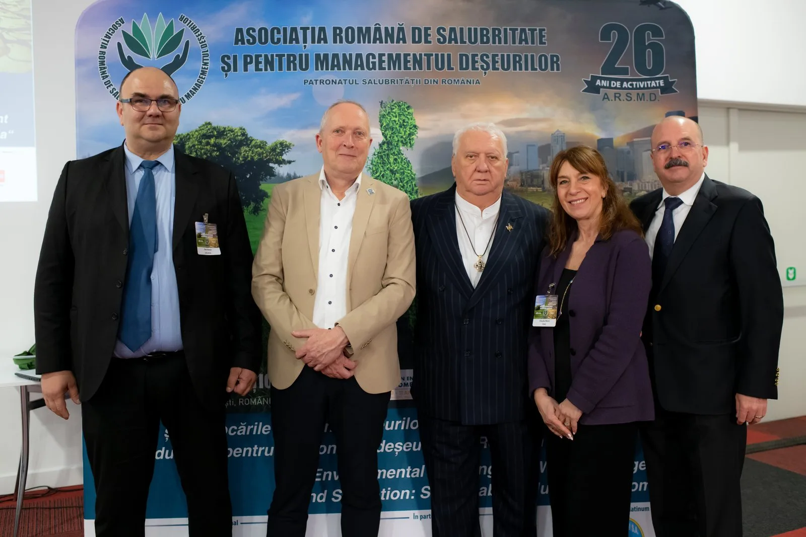 Grup de participanți în fața panoului aniversar „26 de ani de activitate” al A.R.S.M.D.